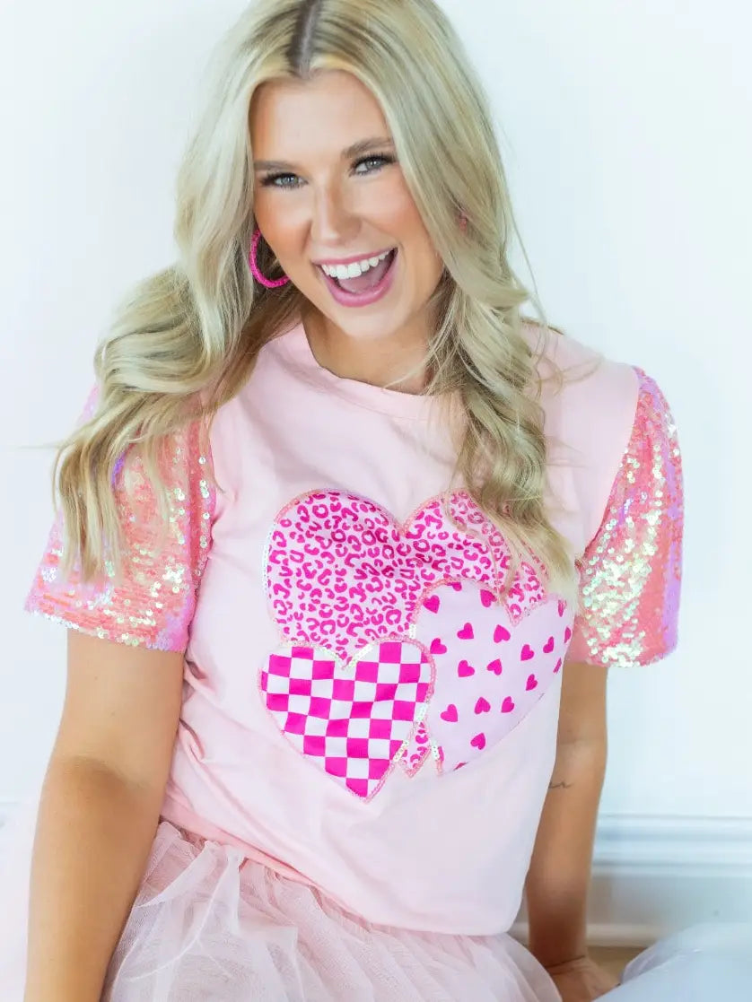 Sequin Sleeve Top is a playful and chic piece that stands out in any wardrobe. Featuring dazzling sequin-lined sleeves and a bold heart graphic.