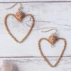 Heart-shaped earrings on a light wooden surface with a soft pink flower.