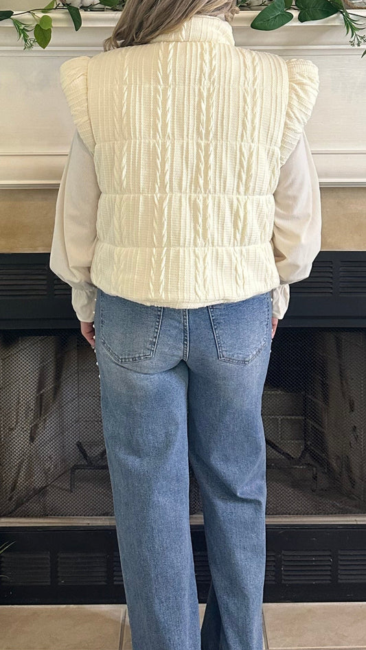 Person wearing a white sweater and blue jeans standing in front of a fireplace.