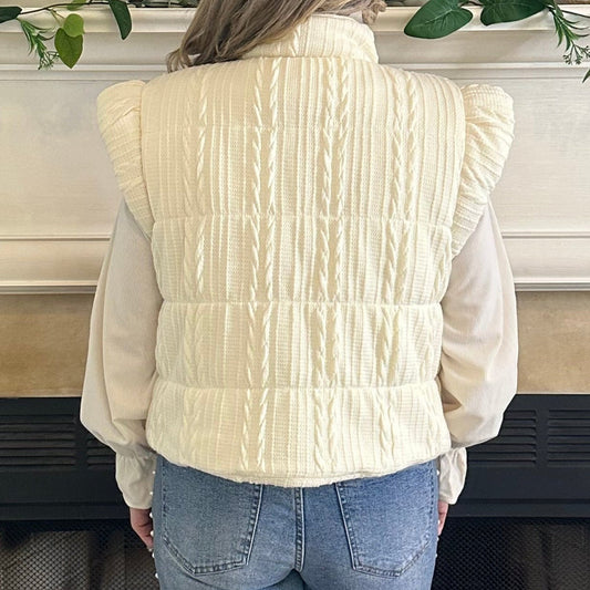 Person wearing a white sweater and blue jeans standing in front of a fireplace.