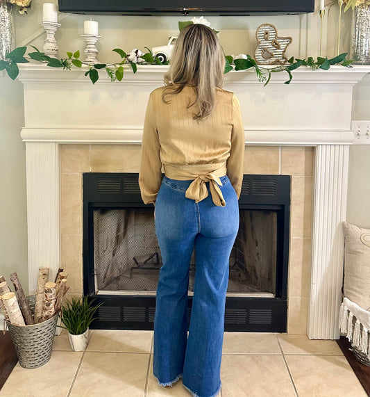Woman standing in front of a fireplace wearing a beige top and blue jeans.