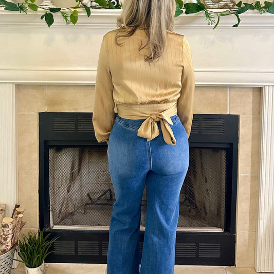 Woman standing in front of a fireplace wearing a beige top and blue jeans.