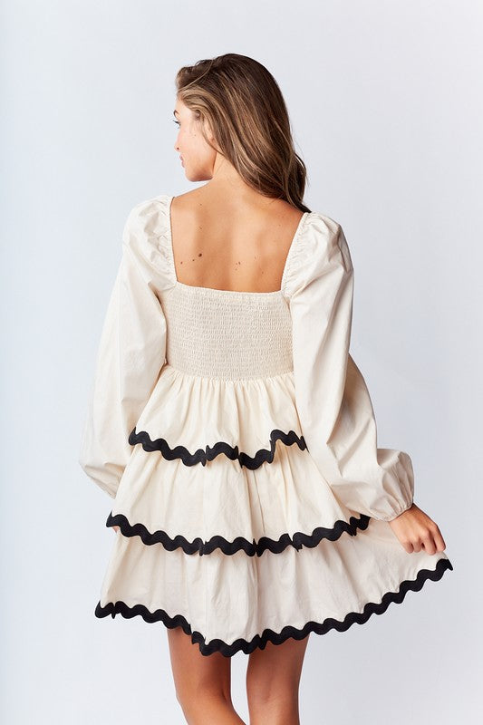 Ric-Rac Mini Dress is a playful and feminine piece that exudes effortless charm. Featuring a deep V-neck with a ribbon tie closure.