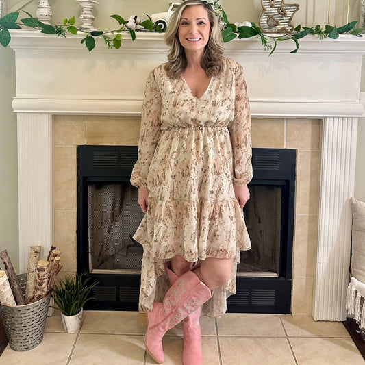 Woman in a floral dress and pink boots standing in front of a fireplace.