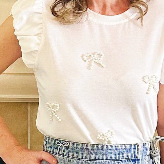 A woman stands in front of a fireplace wearing a white ruffled short-sleeve top, a light blue denim wrap mini skirt, and white cowboy boots. The fireplace mantel has holiday greenery and decorations.