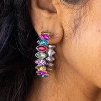 Woman wearing colorful earrings with a pink sequined top against a neutral background