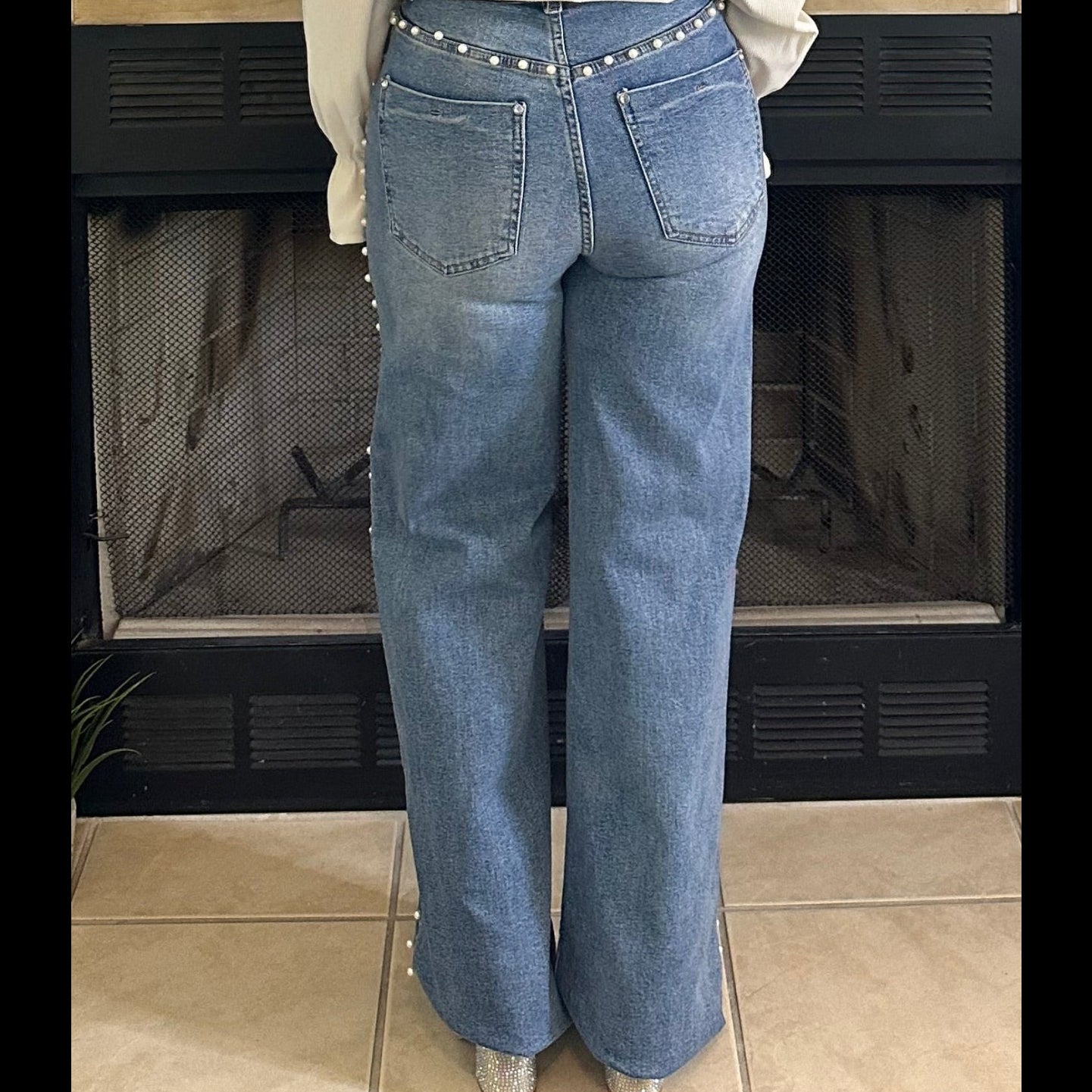 Person wearing blue jeans standing in front of a fireplace.