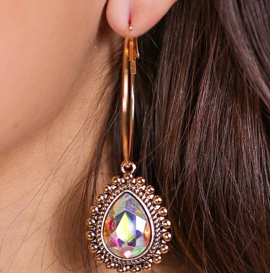 Close-up of a person wearing a rose gold earring with a colorful gemstone.