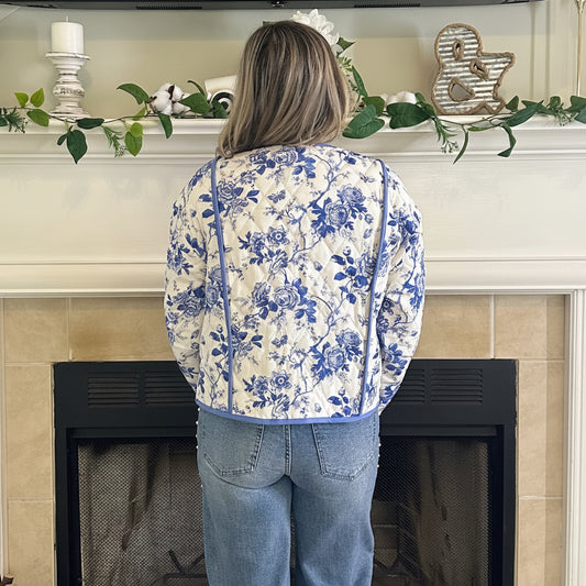 Person wearing a floral hoodie and jeans standing in front of a fireplace.
