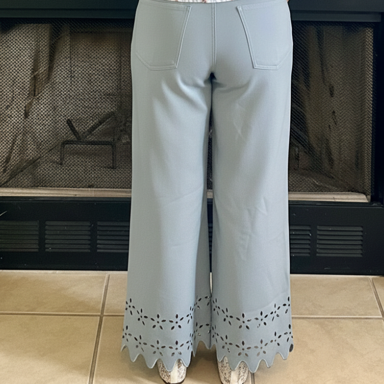 Person wearing light blue pants with scalloped hem in front of a fireplace.