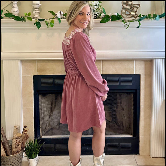 Woman in a pink dress standing in front of a fireplace with decorative elements.