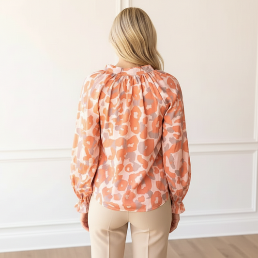 Woman wearing an orange floral blouse and beige pants in a room with white paneled walls.