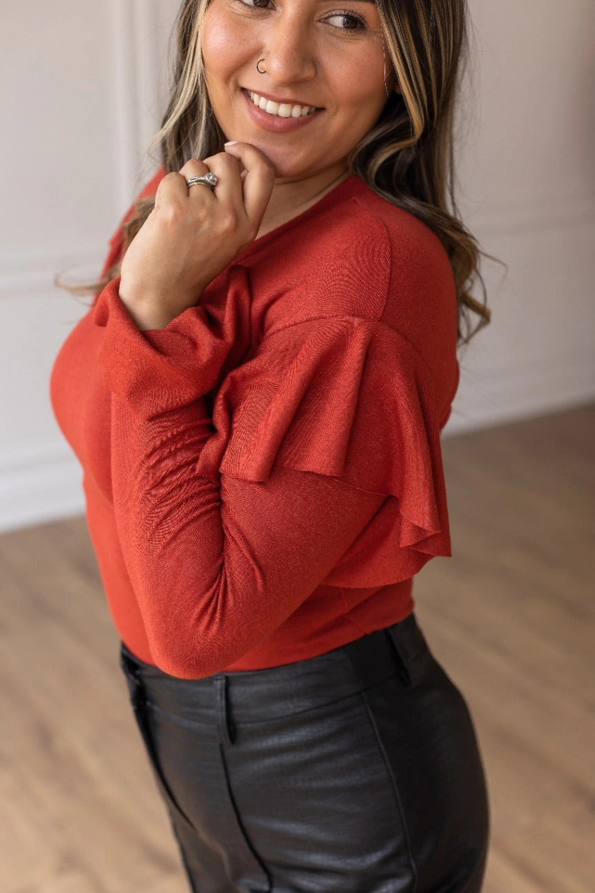 Rust  Ruffle Bodysuit, featuring a sleek, shimmering black fabric that perfectly balances boldness and grace. The cascading ruffle sleeves and flared cuffs create a dramatic silhouette.