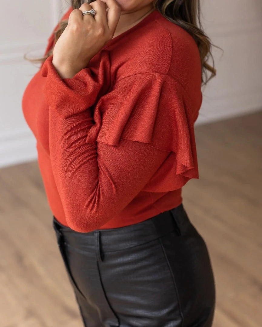 Rust Ruffle Bodysuit, featuring a sleek, shimmering black fabric that perfectly balances boldness and grace. The cascading ruffle sleeves and flared cuffs create a dramatic silhouette.