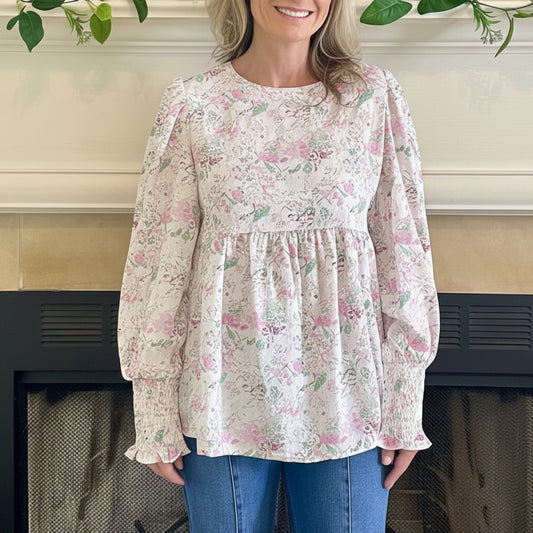 Woman wearing a floral blouse standing in front of a fireplace.