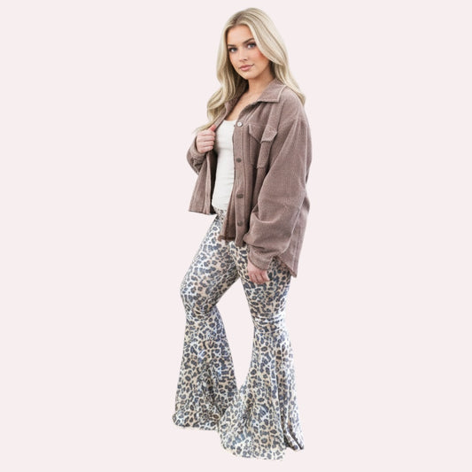 Woman wearing a brown jacket and patterned pants standing against a white wall.