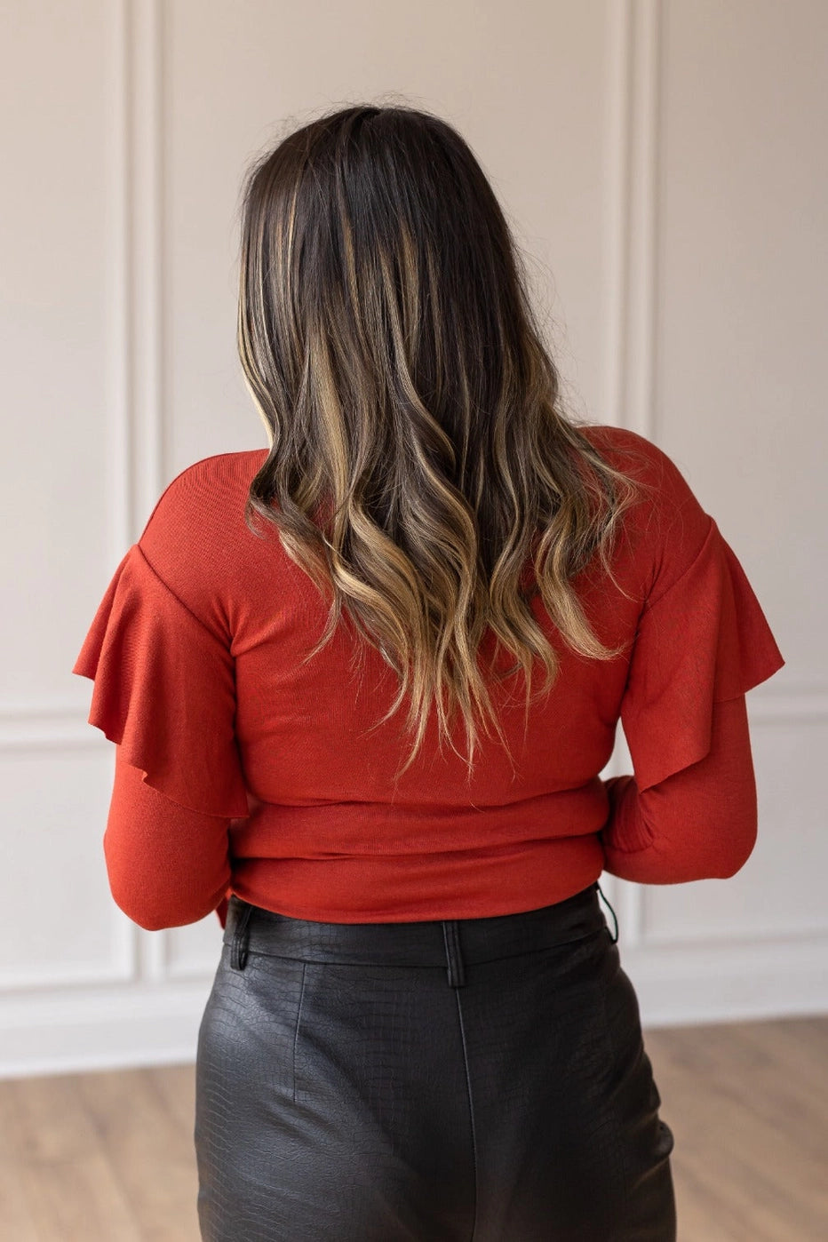 Rust  Ruffle Bodysuit, featuring a sleek, shimmering black fabric that perfectly balances boldness and grace. The cascading ruffle sleeves and flared cuffs create a dramatic silhouette.
