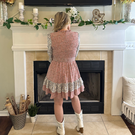 Woman in a floral dress standing in front of a decorated fireplace.