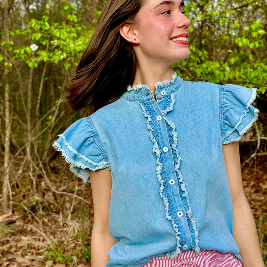 Woman wearing a blue denim top with ruffled sleeves and white buttons, standing outdoors.