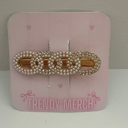 A gold-tone hair claw clip embellished with white faux pearls, displayed on a pink card labeled 'TRENDY MERCH' against a neutral gray background.