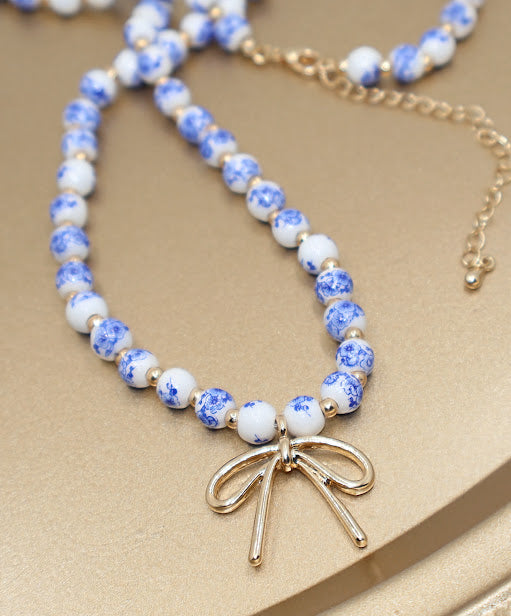 Necklace with blue and white bead design and gold bow charm.
