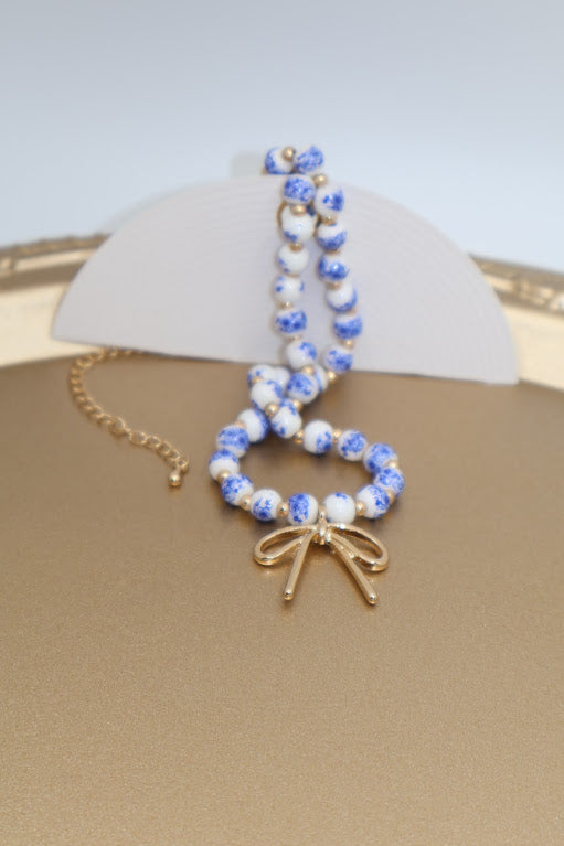 Beaded bracelet with a gold bow charm on a beige surface