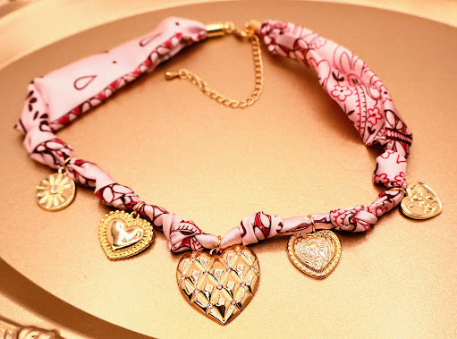 Necklace with pink fabric and gold heart charms on a beige background