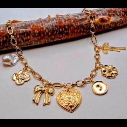 This exquisite necklace features a delightful array of charms, including a metal heart, a charming bow, a floral quatrefoil, and lustrous pearl accents.