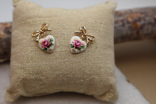 These sweet and dainty heart-shaped drop earrings feature a delicate floral print complemented by polished gold bow studs.