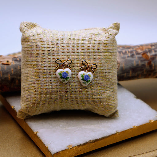 Heart-shaped earrings with floral designs on a textured pillow