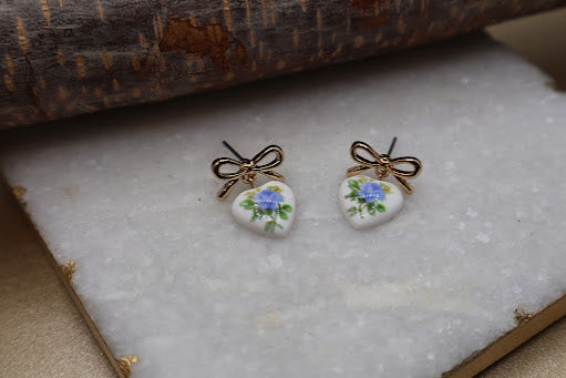 Pair of earrings with floral design and gold bows on a textured surface