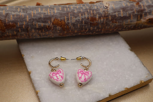Pair of earrings with pink floral design on a white stone surface.