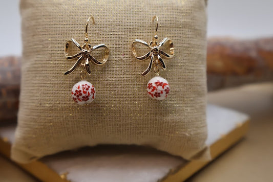 These earrings feature a stunning metal bow design paired with beautifully crafted ceramic balls adorned with a vibrant red floral pattern.