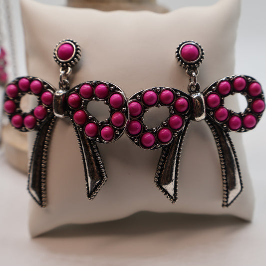 Pink bow-shaped earrings on a white cushion
