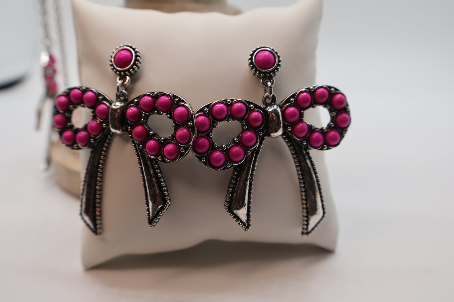 Pink bow-shaped earrings on a white cushion
