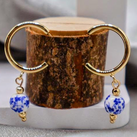 Pair of earrings with blue and white floral designs on a wooden block