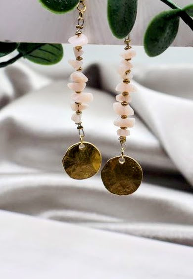 Earrings with pink beads and gold disc charms on a white fabric background