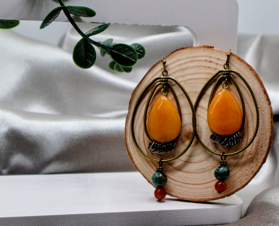 Pair of orange teardrop earrings with green and red beads on a wooden stand.
