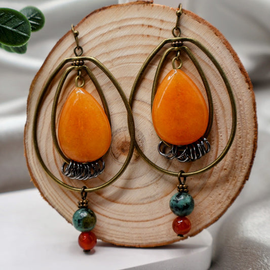 A pair of Boho earrings featuring intricate dangling detailed pendants, these lightweight earrings are designed for comfort and style. The unique oval wire design adds a modern touch, while the vibrant colors make them perfect for any occasion. Measuring 3 inches in length, these earrings are sure to make a statement without weighing you down.