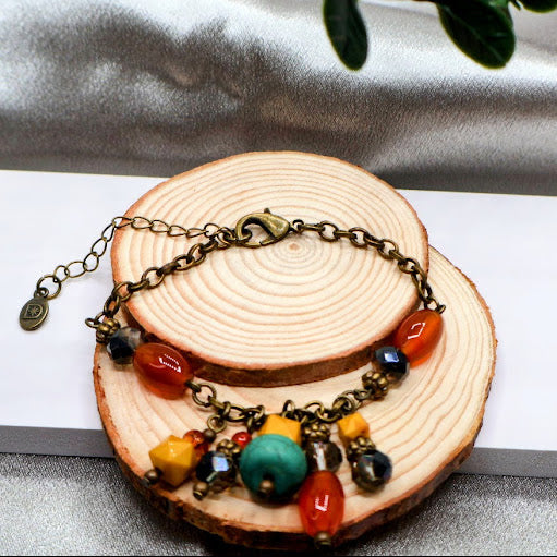 Bracelet with colorful beads and charms on a wooden slice with a plant in the background