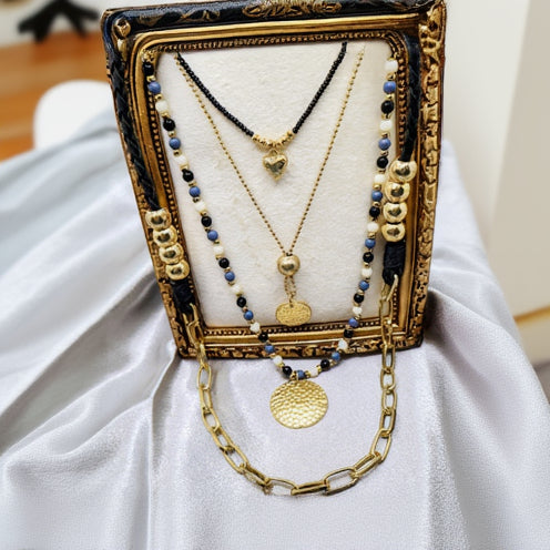 Set of gold and beaded necklaces on a decorative stand with a white fabric background