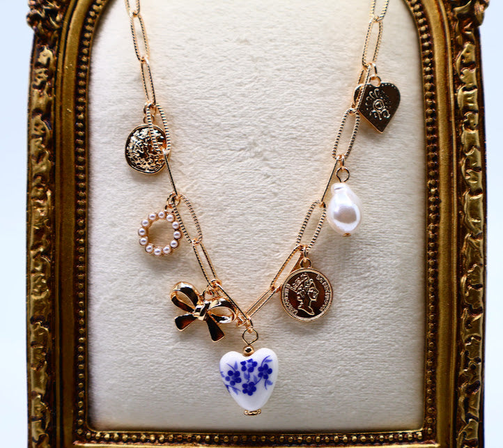 Charm Necklace. This gold-tone necklace features a combination of unique, eye-catching charms, including a delicate pearl, a floral-inspired heart, and intricate coin pendants.