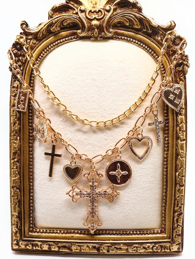 Charm Necklace. This beautifully layered gold-tone necklace features an enchanting collection of delicate charms, including graceful hearts, intricate crosses, and classic coin pendants. The centerpiece, a stunningly detailed cross.