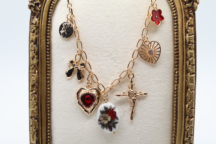 Vintage Charm Necklace. Featuring a gold-tone chain adorned with an exquisite collection of charms, including a rose-adorned heart, a dainty bow, a floral oval pendant, and a radiant cross.