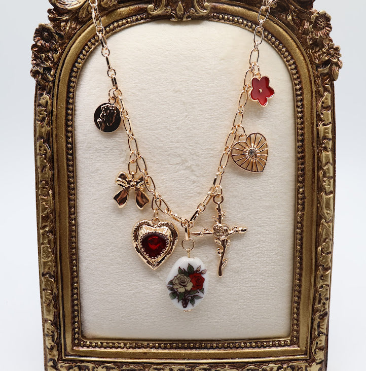 Vintage Charm Necklace. Featuring a gold-tone chain adorned with an exquisite collection of charms, including a rose-adorned heart, a dainty bow, a floral oval pendant, and a radiant cross.