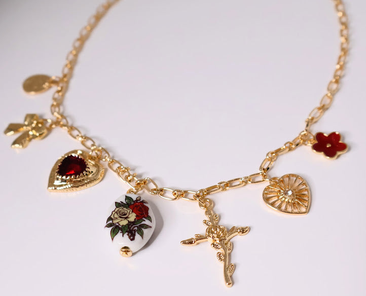 Vintage Charm Necklace. Featuring a gold-tone chain adorned with an exquisite collection of charms, including a rose-adorned heart, a dainty bow, a floral oval pendant, and a radiant cross.