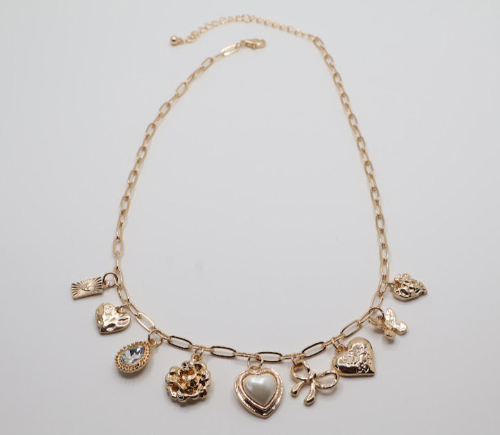 Charm Necklace.  Featuring a delicate gold-tone chain adorned with an array of feminine charms, including a pearl heart, a dainty bow, sparkling crystals, and floral motifs.