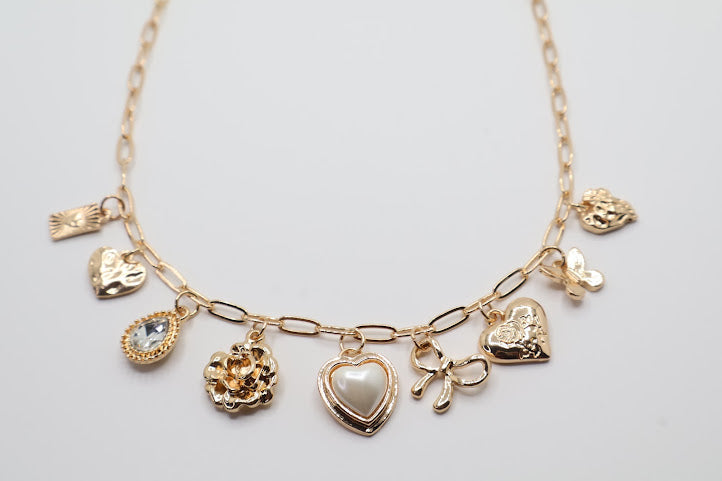 Charm Necklace.  Featuring a delicate gold-tone chain adorned with an array of feminine charms, including a pearl heart, a dainty bow, sparkling crystals, and floral motifs.