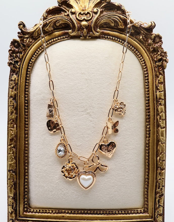 Charm Necklace.  Featuring a delicate gold-tone chain adorned with an array of feminine charms, including a pearl heart, a dainty bow, sparkling crystals, and floral motifs.