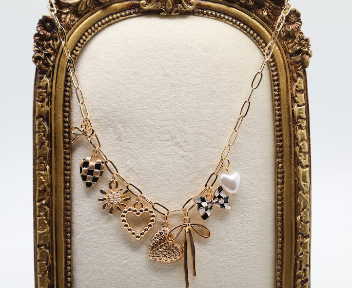 Charm Cascade Necklace  Featuring a gold-tone chain adorned with charming pendants, including textured hearts, a delicate bow, a luminous pearl, and checkered-inspired accents.
